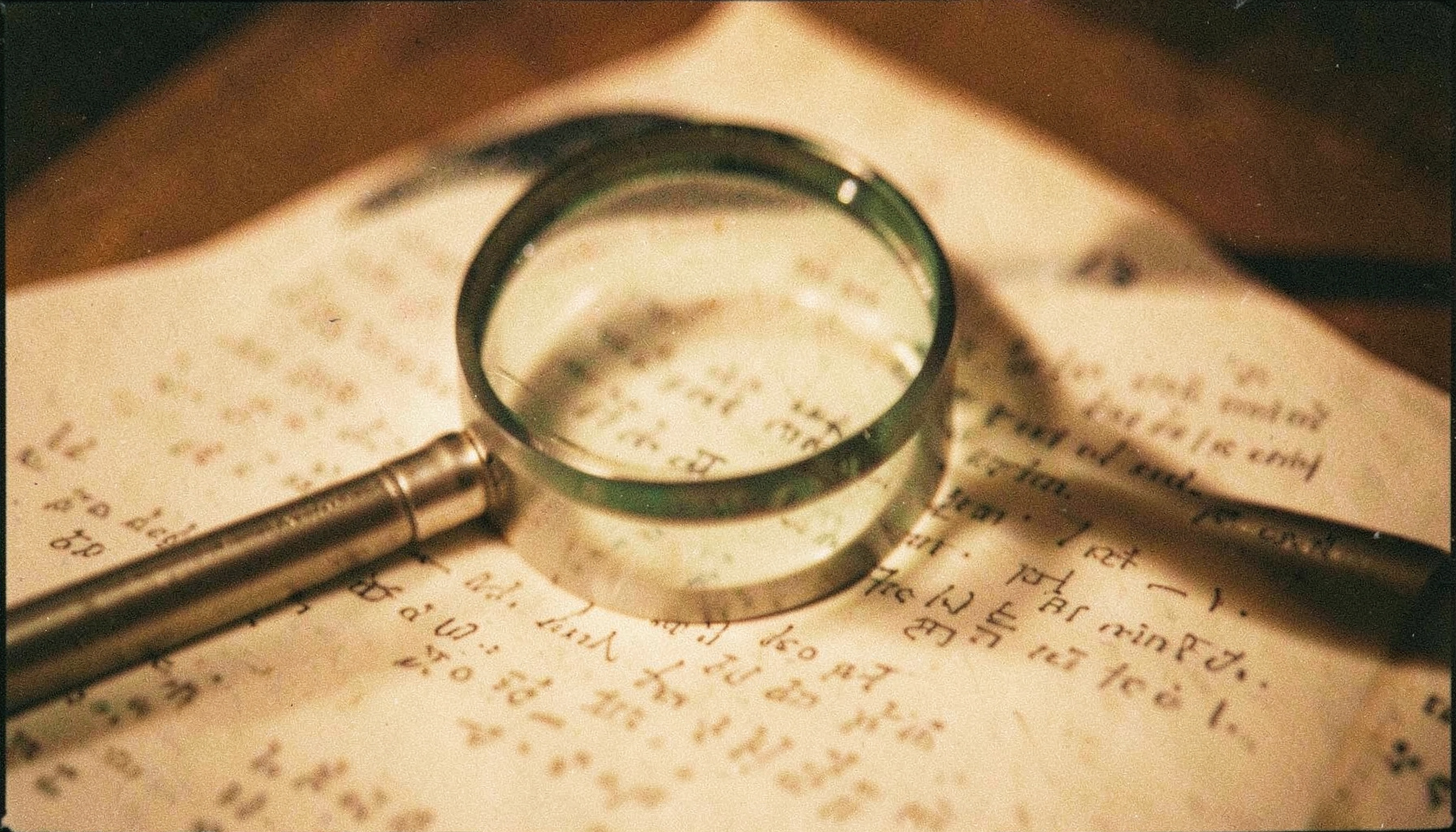 A close-up analog film photograph of a magnifying glass resting on a printed document, warm amber and cream tones with visible grain